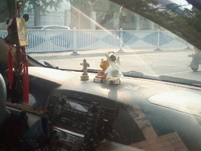 Buddhist monk doing Tai Chi, a pig (with devil horns?), and a Christian angel with halo - random stuff on a random dashboard in Nanning, Guangxi Province, China, summer 2012.
