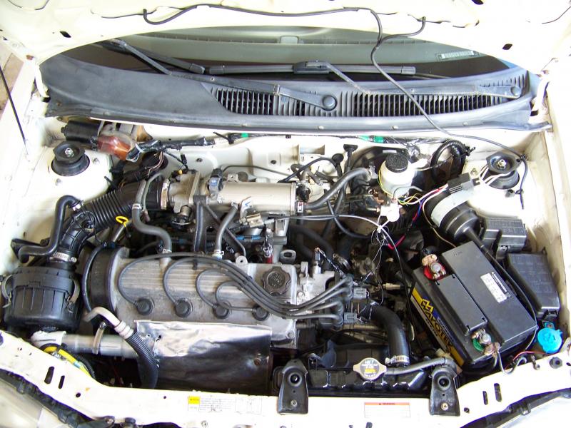 Overview of the engine bay, where you can see the installed warm air intake system.

It's simply made out of a PVC elbow, muffler adapters and an aluminum sheet.

Also you can see at your right hand side (left hand side of the car), near the shock absorber tower, the modified Audiovox (CCS-100) MPG Sensitive Cruise Control Servomotor. Also the Ignition Kill Relay.