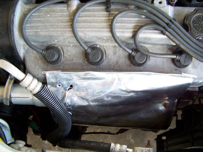 A closer view of the aluminum sheet and one of the 3 bolts that holds it in place. This cover forces the warm air to the intake tube extension. The original manifold shroud was removed and the aluminum sheet was bolted in place.

This also serves to reflect radiant heat back to the manifold raising the temperature for the catalytic converter and keeping the A/C condenser a bit more cooler.