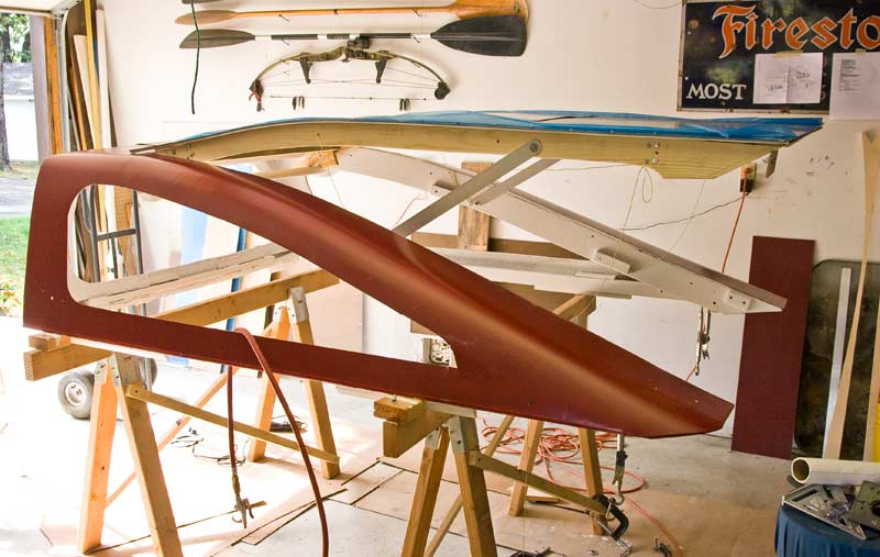 During construction with hatch raised.  The aluminum bar stock supports are hinged to drop when raised.  A notch in the ends catches on a 1/4" bolt clamped to the side of the shell.  Kevlar cord stops will keep the hatch from raising too far, either by operator error or wind gust.  A second cord is looped through the bars to  pull them up when it's time to lower the hatch.  I had originally found some used gas cylinders but my wood framing was nowhere near strong enough to stand the stress.